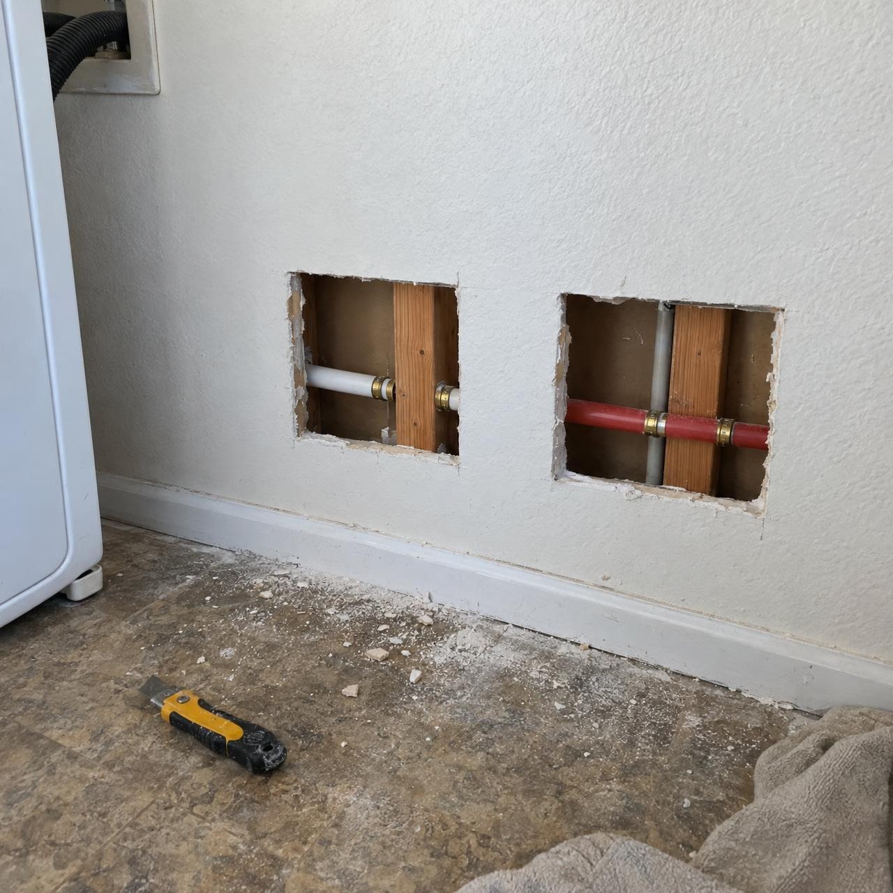 Access holes cut in a laundry room wall to reach the pipes